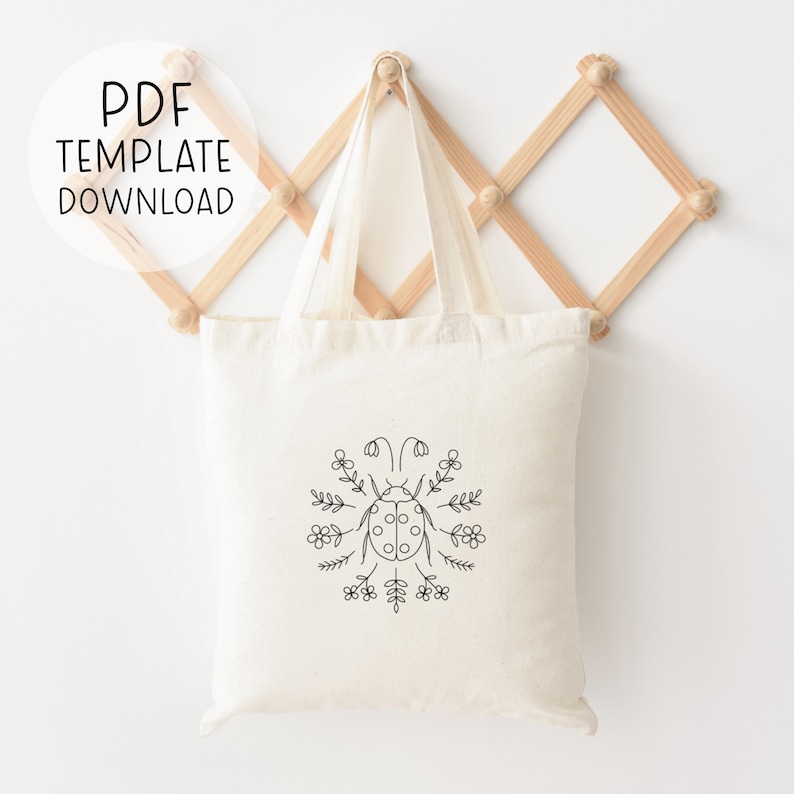 Puede incluir: Una bolsa de lona blanca con un dibujo de l&iacute;nea negra de una mariquita rodeada de flores. El texto "PDF TEMPLATE DOWNLOAD" est&aacute; en un c&iacute;rculo en la parte superior de la imagen.