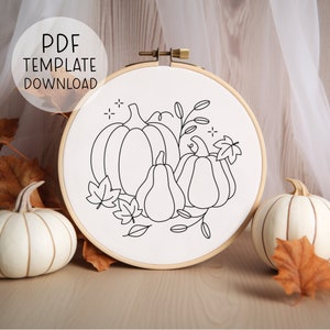 Peut inclure: Un dessin au trait noir et blanc de citrouilles et de feuilles sur un fond blanc à l'intérieur d'un cerceau de broderie en bois.