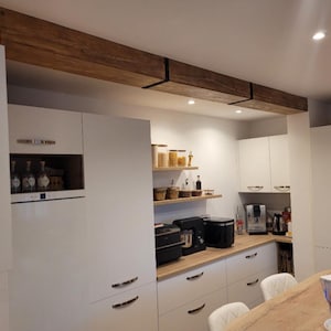 Puede incluir: Una cocina moderna con gabinetes blancos, encimeras de madera y una viga de madera en el techo. Los electrodomésticos incluyen un microondas, una cafetera y una tostadora. Estantes exhiben frascos y botellas. La cocina tiene una estética brillante y limpia.