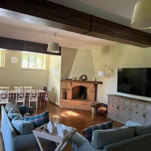 Può includere: Un soggiorno con due divani grigi con cuscini a quadri, un tavolino in legno, un camino in mattoni e una televisione montata sopra un mobile grigio. Sullo sfondo si vede una zona pranzo con una tovaglia a quadri e sedie bianche.