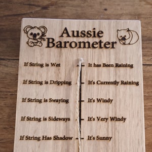 Puede incluir: Señal de madera con una cuerda colgando, etiquetada como "Aussie Barometer". La señal tiene un koala y un wombat. La cuerda se utiliza para determinar el clima. Si la cuerda está mojada, ha estado lloviendo. Si la cuerda está goteando, está lloviendo actualmente. Si la cuerda se balancea, hace viento. Si la cuerda está de lado, hace mucho viento. Si la cuerda tiene sombra, hace sol. Si la cuerda no tiene sombra, está nublado.