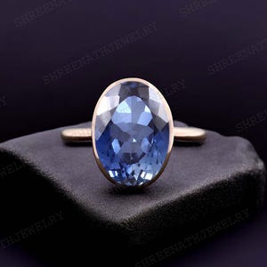 May include: A blue oval gemstone ring set in a rose gold band. The ring is on a black velvet surface.