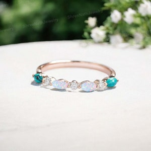 Op de afbeelding: Een delicate ring van roségoud met vijf ovale edelstenen. De middelste drie stenen zijn witte opalen en de twee buitenste stenen zijn turquoise.