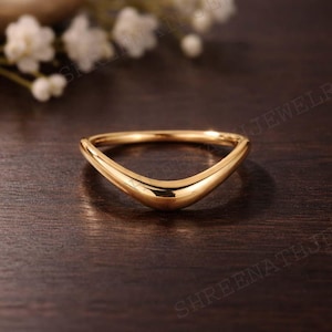 Pode incluir: Um anel dourado curvo com uma superfície lisa e polida. O anel tem um design em forma de V, com um topo arredondado e uma estética elegante e moderna. O anel é provavelmente feito de metal e é adequado para uso diário.