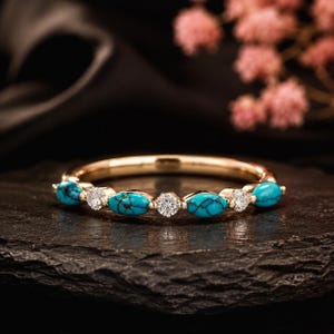 May include: A gold band ring featuring an alternating pattern of four marquise-cut turquoise stones with dark veining and three round-cut clear white stones. The stones are set horizontally along the top half of the polished gold metal band.