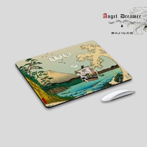 Puede incluir: Alfombrilla de ratón rectangular con una ilustración de estilo japonés de un barco sobre una ola, con una montaña al fondo. La alfombrilla tiene un borde negro y un ratón blanco está al lado. El texto "Angel Dreamer" está en la esquina superior derecha.