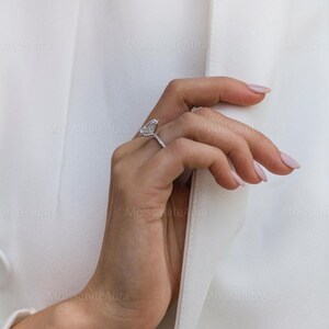May include: A close-up of a hand wearing a silver ring with a large, clear, heart-shaped diamond. The ring is set in a simple band.
