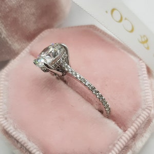 Pu&ograve; includere: Un anello di fidanzamento in argento con una grande pietra centrale rotonda e una fascia di diamanti pi&ugrave; piccoli.