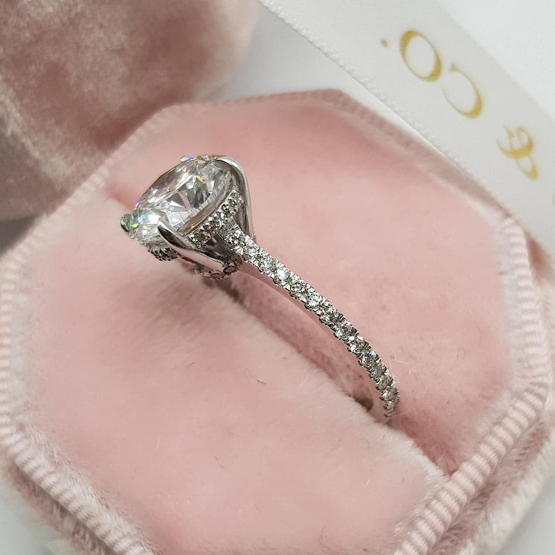 Pu&ograve; includere: Un anello di fidanzamento in argento con una grande pietra centrale rotonda e una fascia di diamanti pi&ugrave; piccoli.