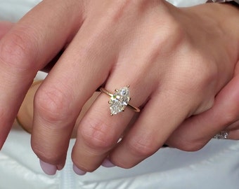 May include: A gold ring featuring a marquise-cut diamond. The diamond is set on a thin gold band. The ring is shown on a person's hand.