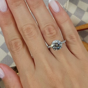 Pu&ograve; includere: Un anello di fidanzamento in argento con un grande diamante rotondo centrale e diamanti pi&ugrave; piccoli incastonati in una fascia pav&eacute;.