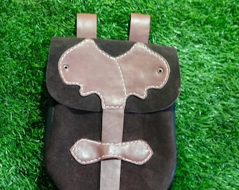 Op de afbeelding: Een bruine leren tas met een klep en een riem. De tas heeft een decoratief ontwerp aan de voorkant en is gemaakt van suède.