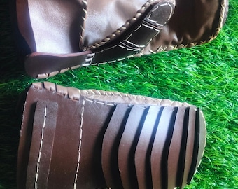 May include: A pair of brown leather archery finger guards with white stitching. The guards have a textured design on the back.