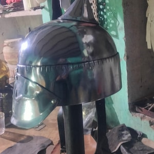 May include: A silver helmet with a pointed top and a leather strap. The helmet is on a wooden stand and there are pieces of leather on the table.
