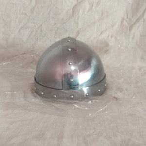 May include: A silver helmet with a rounded dome and a band of rivets around the bottom edge. The helmet is made of metal and has a smooth, shiny finish.