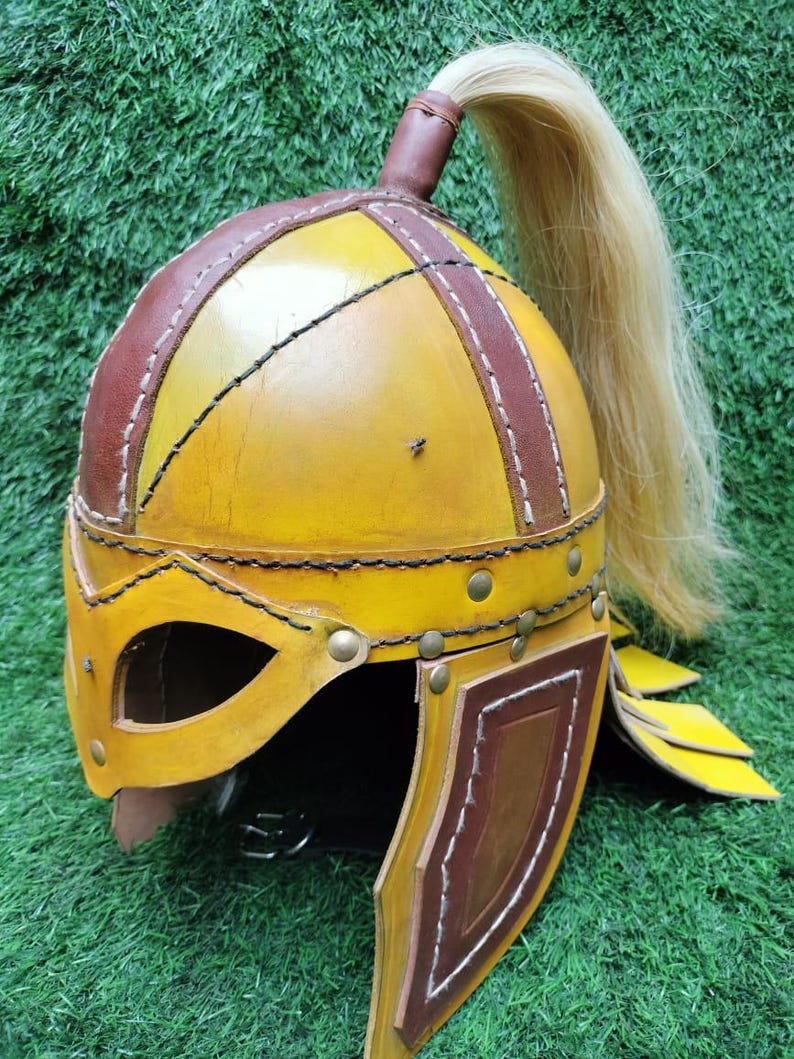 May include: A yellow leather helmet with brown leather accents and a long blonde hairpiece. The helmet has a face mask and ear flaps.