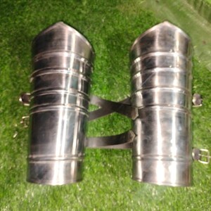 May include: A pair of silver metal arm guards with straps. The guards are cylindrical and have a slightly pointed top.