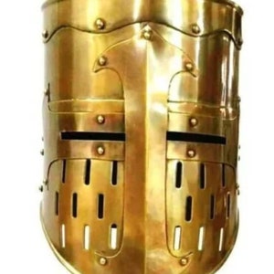 May include: A gold knight's helmet with a visor and a faceplate featuring a cross design. The helmet has a textured surface and is made of metal.