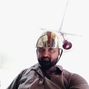 May include: A man wearing a gold helmet with a serious expression. He is wearing a brown polo shirt with a logo on the front.