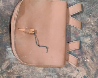 May include: A brown leather pouch with a flap closure and three leather straps. The pouch has a small loop on the front.