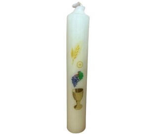 May include: A tall, off-white candle with religious symbols. The candle features a wheat stalk, a cross, a bunch of grapes, and a chalice. The candle is a religious item, likely for a ceremony.