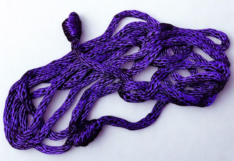May include: A close-up shot of a length of purple rope, intricately woven with a textured pattern. The rope is a deep, rich shade of purple, with darker accents. The rope is knotted at one end.