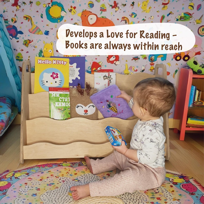 Może przedstawiać: Jasna drewniana p&oacute;łka na książki wypełniona książkami dla dzieci, w tym książką Hello Kitty. Tekst "Develops a Love for Reading - Books are always within reach" jest wyświetlany powyżej. Dziecko siedzi na podłodze, sięgając po książkę.