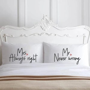 May include: Two white pillowcases with black script that reads "Mrs. Always right" and "Mr. Never wrong", each with a small red heart. The pillows are on a bed with a white headboard.