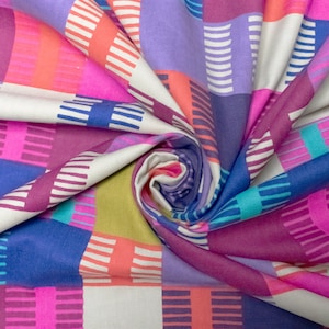 Op de afbeelding: Close-up van een kleurrijke stof met een geometrisch patroon. Het ontwerp bevat vierkanten in tinten roze, paars, blauw, oranje en groen, met witte gestreepte accenten. De stof is gevouwen en gedraaid, wat de levendige kleuren en het ontwerp laat zien.