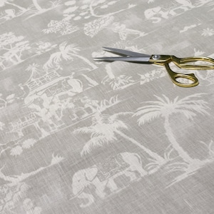 以下が含まれることがあります： グレーの生地のクローズアップ。白いヤシの木、ゾウ、パゴダが繰り返しパターンで描かれています。銀色のハサミが生地の上に置かれています。