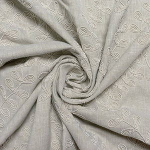 Könnte beinhalten: Nahaufnahme eines hellgrauen Stoffes mit einem weißen, gestickten Blumenmuster. Der Stoff ist gefaltet und strukturiert.