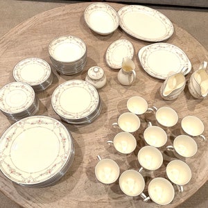 Puede incluir: Un juego de vajilla de porcelana fina blanca con un patrón floral. El juego incluye platos, tazones, tazas y platillos.