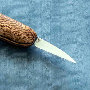 May include: A close-up of a small, wooden-handled knife with a thin, sharp blade. The blade is made of stainless steel and has a slight curve to it. The handle is made of dark wood with a light wood inlay. The knife is lying on a blue surface.
