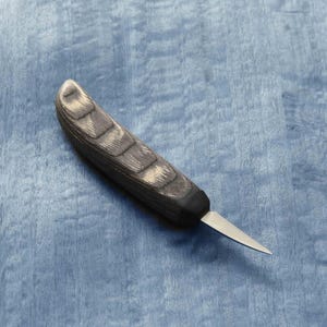 May include: A small, black and grey wood handled carving knife with a thin, sharp blade. The knife is lying on a blue surface.