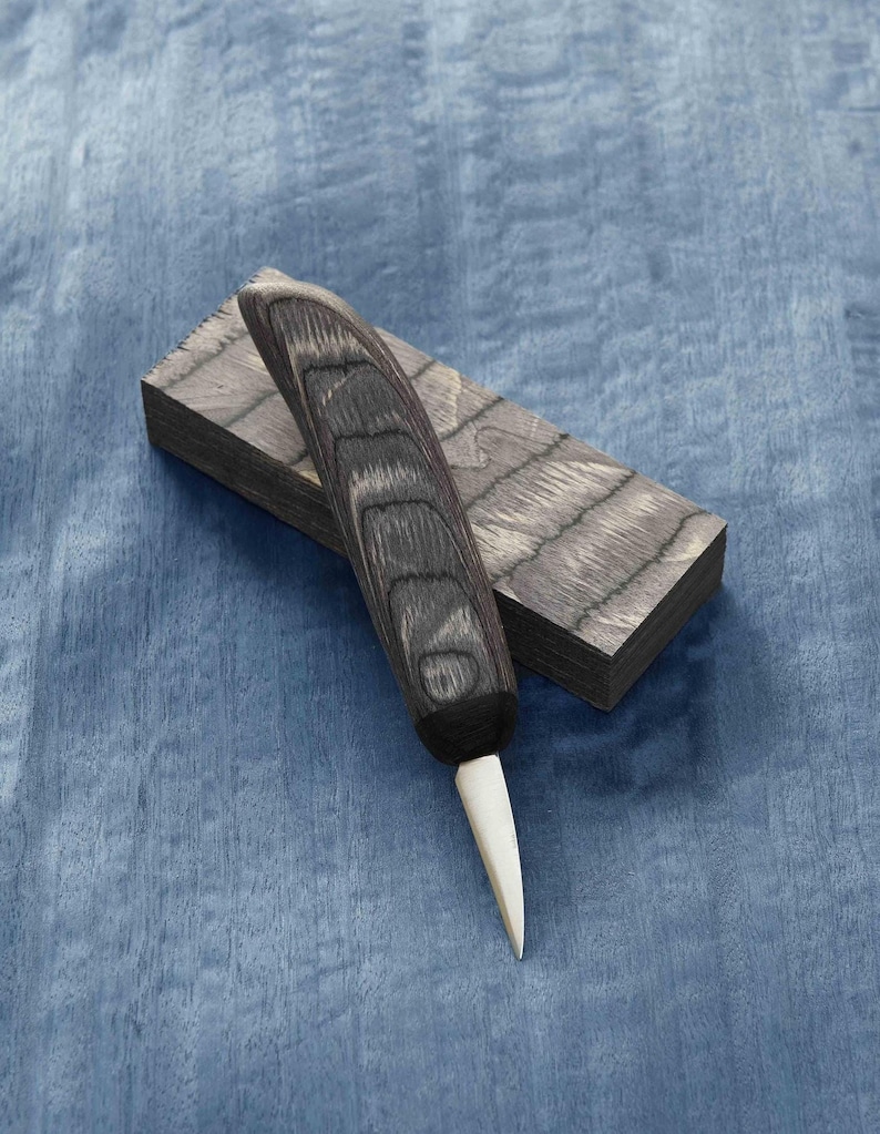 High Carbon Wood Carving Knife with 1 1/2 inch blade. Crafted using d2 steel. The ergonomic flat handle is made of laminated colored wood planks. The 3mm unpainted natural leather sheath is carefully stitched by hand. You will enjoy this knife.