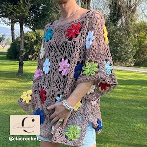 Pode incluir: Um top de crochê marrom adornado com aplicações de flores coloridas. O top tem um design solto e aberto com mangas curtas. A imagem também inclui o texto "C @clacrochet".