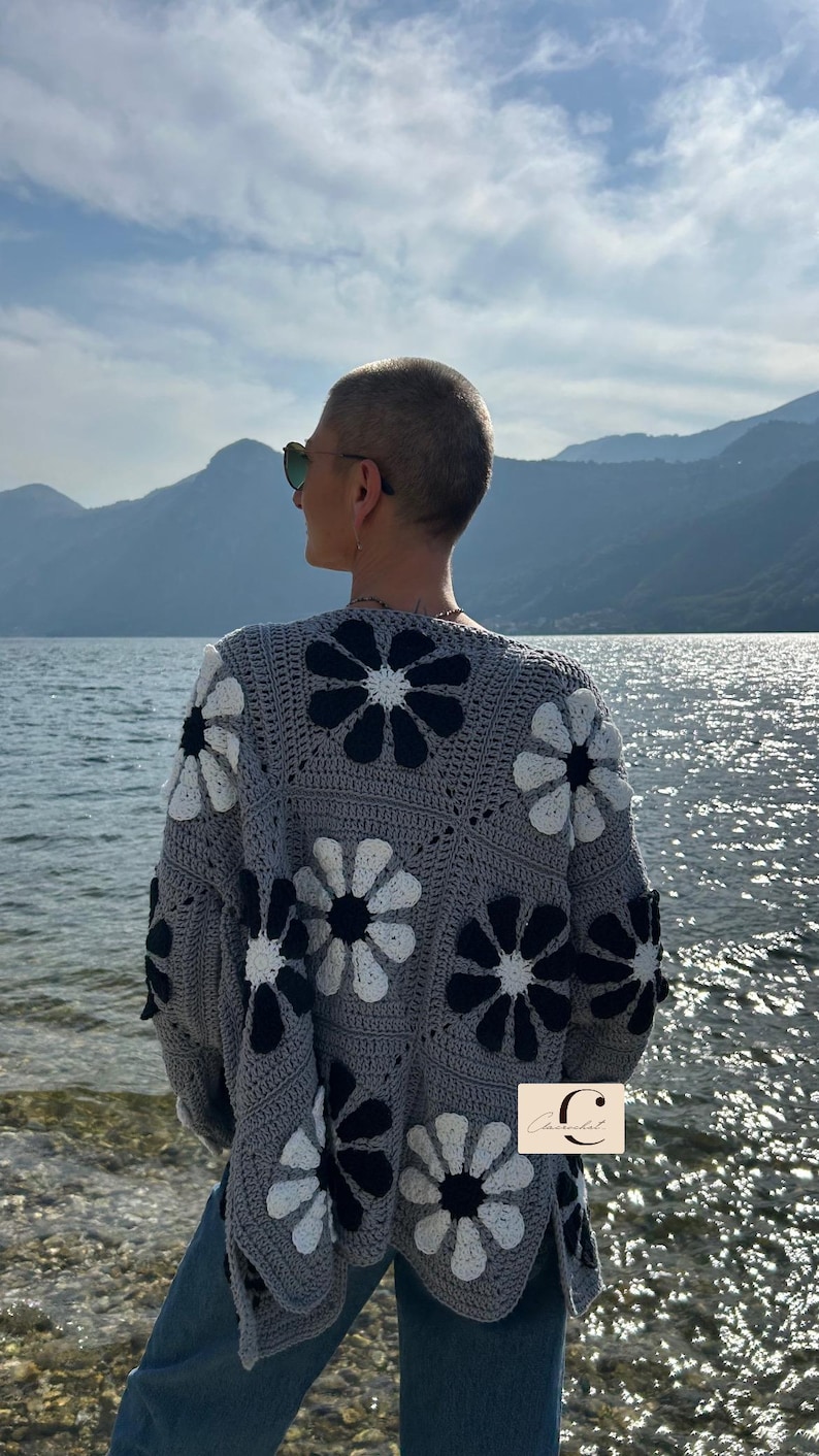 May include: A gray crocheted cardigan with a black and white daisy pattern. The cardigan has a relaxed fit and long sleeves.