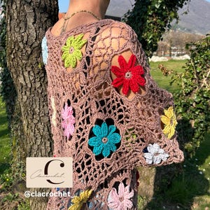 May include: A brown crochet top with colourful, three-dimensional flower appliqu&eacute;s. The open-weave design features flowers in shades of red, yellow, blue, pink, green, and white. The Etsy shop name "clacrochet" is visible in the lower left corner.