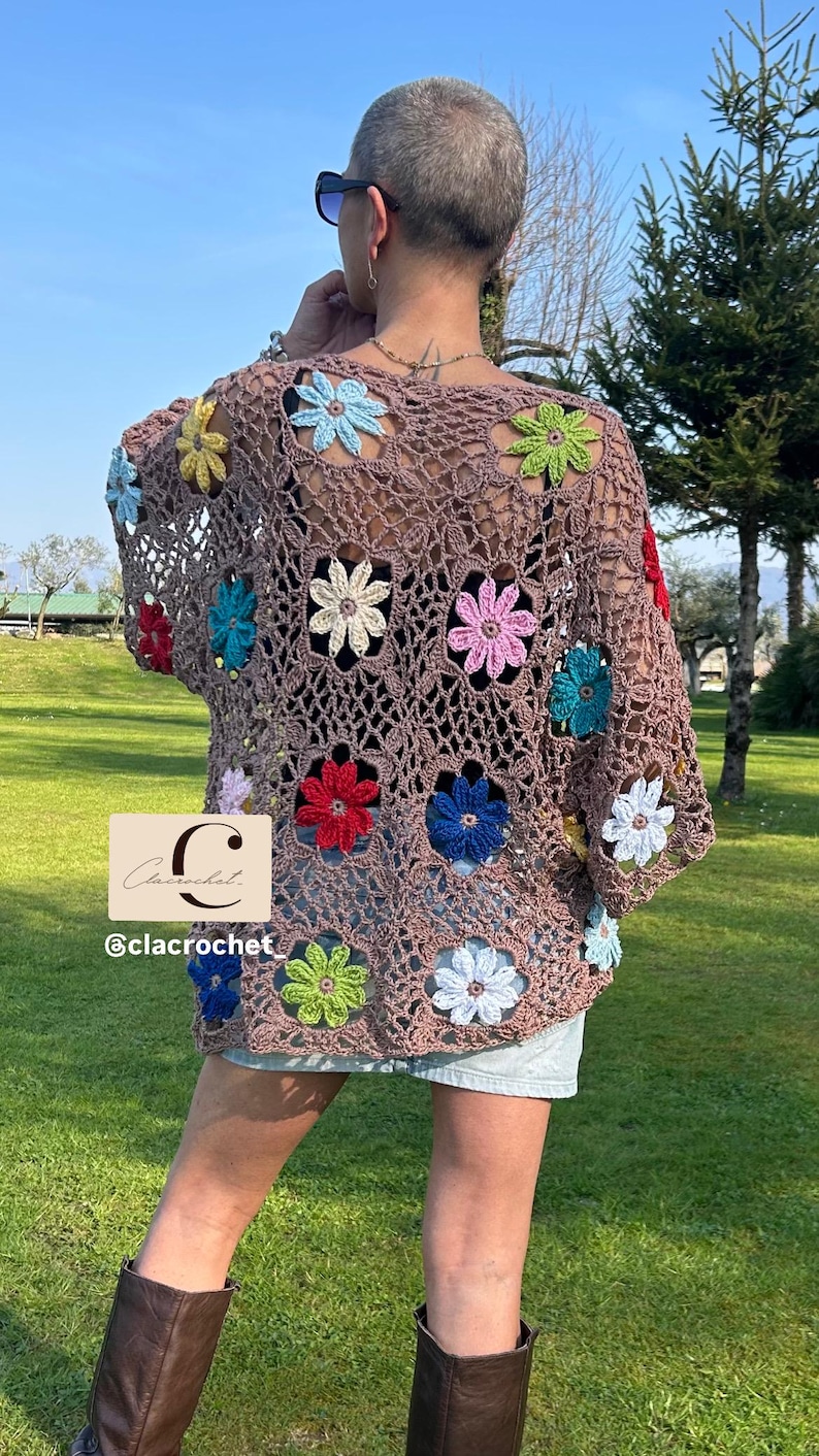 May include: A brown crochet top with colourful flower appliqu&eacute;s. The open-weave design features flowers in red, blue, green, and pink. The top is worn with denim shorts and brown boots, creating a bohemian aesthetic.