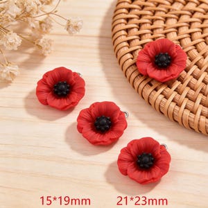 May include: Four red poppy flower charms with black centers. Two charms measure 15 x 19 mm, and two measure 21 x 23 mm. The charms have a silver-colored loop for attaching to jewelry or other crafts.