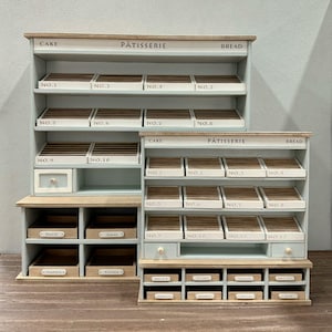 Può includere: Mini scaffali da esposizione per panetteria in tonalità azzurro chiaro e legno. Gli scaffali sono etichettati "Cake", "Pâtisserie" e "Bread". Ogni ripiano ha scomparti numerati per l'esposizione di prodotti da forno. Ulteriori ripiani sottostanti hanno etichette come "Tortilla" e "Scone".