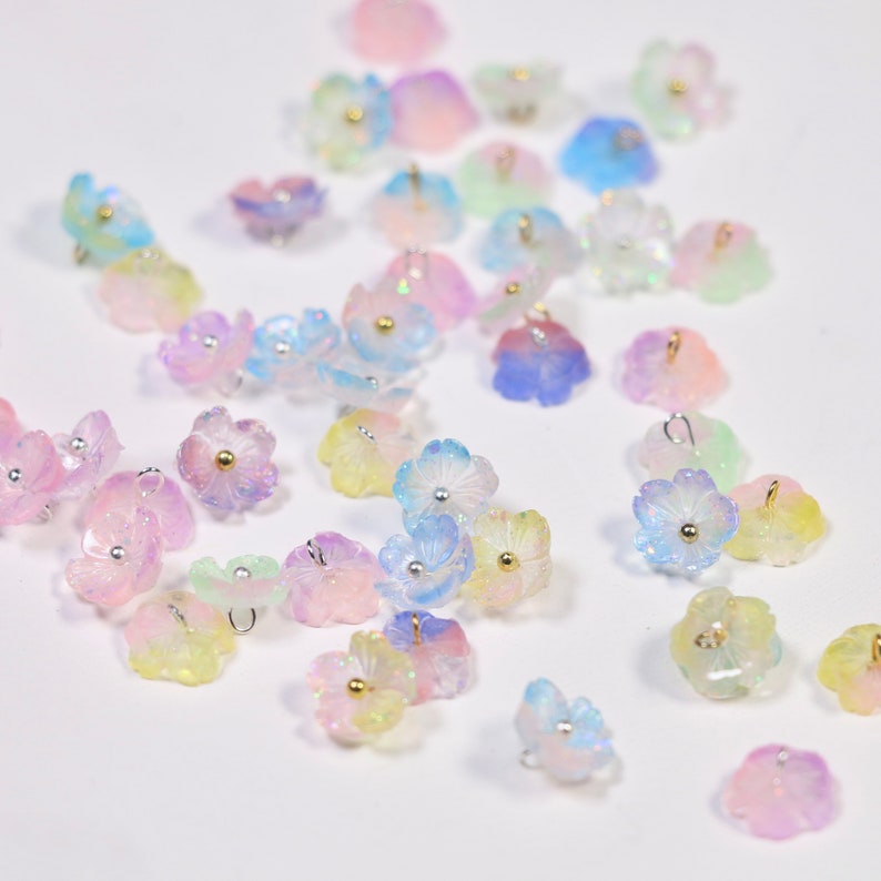 May include: Assortment of iridescent pastel flower charms with gold accents. The charms have a delicate, feminine aesthetic and are perfect for adding a touch of whimsy to jewelry or crafts.