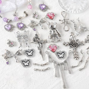 May include: Assortment of silver-toned metal charms with various designs, including butterflies, bows, hearts, crosses, and a robot. Some charms feature pink and purple rhinestones.