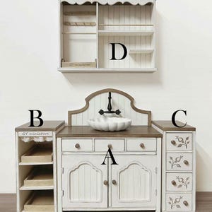 Pu&ograve; includere: Un set da cucina in miniatura bianco e marrone con lavandino, armadietti e una mensola a muro. Il set include un lavandino con un rubinetto nero, cassetti e un armadietto con ante. La mensola a muro ha ganci e ripiani.