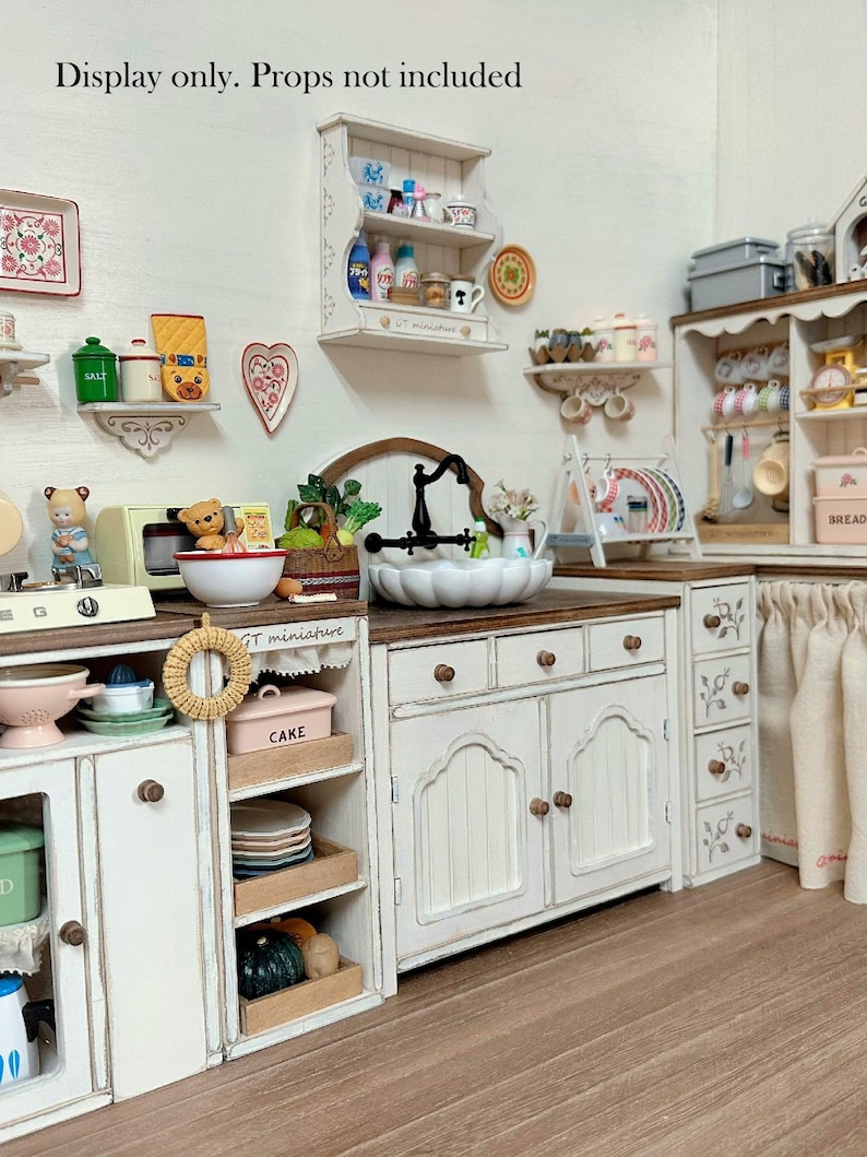 Pu&ograve; includere: Una scena di cucina in miniatura con mobili, mensole e un lavandino bianchi. La scena comprende vari oggetti da cucina in miniatura come piatti, tazze e generi alimentari. Il testo "Display only. Props not included" &egrave; visibile in alto.