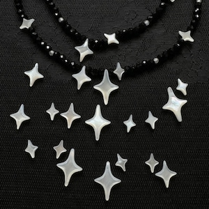 May include: A necklace featuring a strand of small, faceted black beads interspersed with white, four-pointed star-shaped charms. The charms are arranged in a scattered pattern, resembling a night sky, with varying sizes of stars across the piece.
