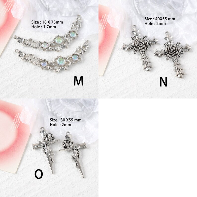 May include: Two silver-toned metal cross charms with a rose design. The cross on the left is 30 mm wide by 55 mm tall. The cross on the right is 40 mm wide by 55 mm tall. Both crosses have a 2 mm hole for attaching to a chain or other jewelry.
