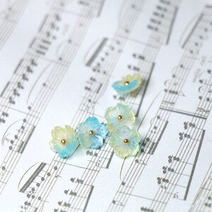 May include: Five pastel blue and yellow flower-shaped resin embellishments with gold accents on a sheet of music.