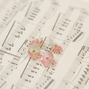 May include: Four pink and white flower-shaped buttons with gold accents. The buttons are on a sheet of music.