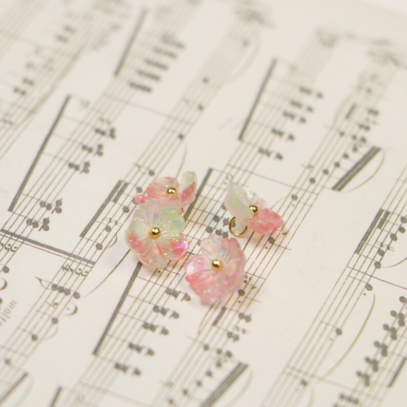 May include: Four pink and white flower-shaped buttons with gold accents. The buttons are on a sheet of music.